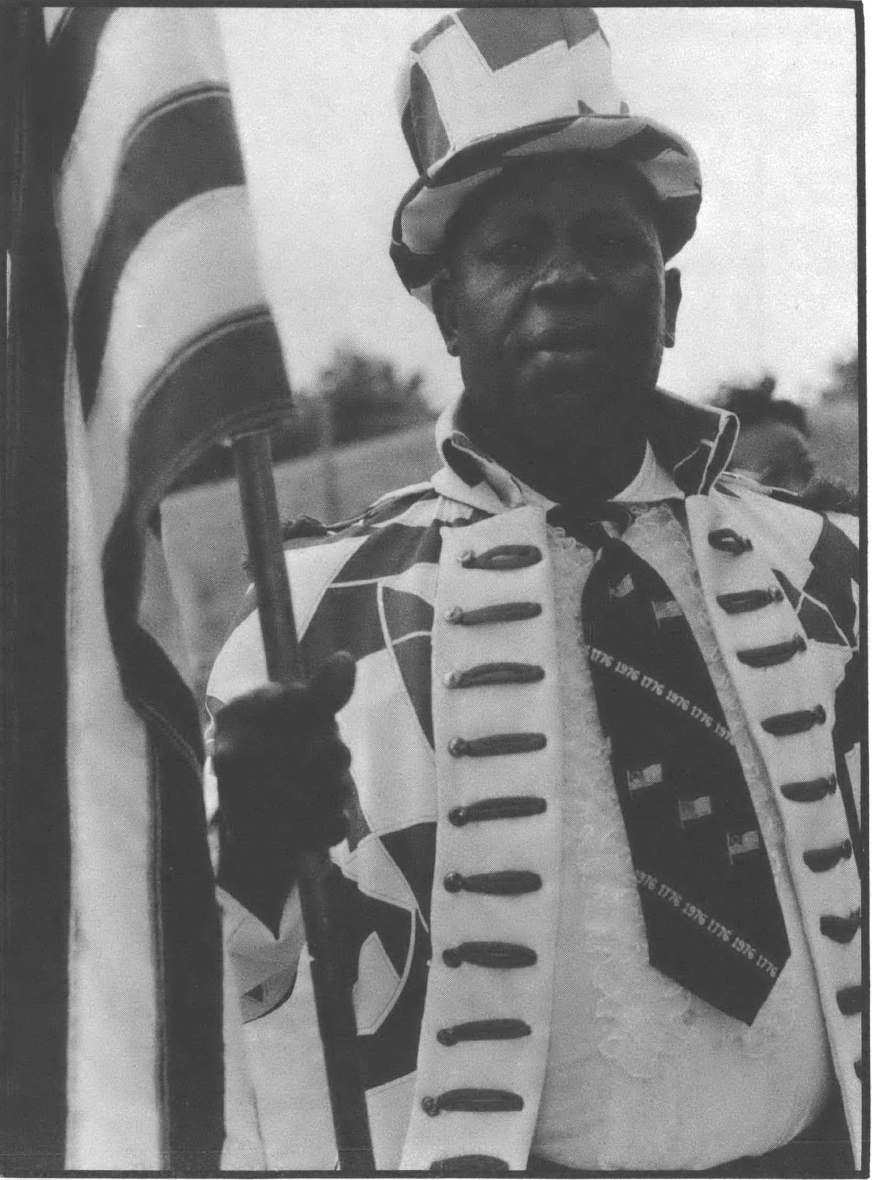 Black and white photo of Black man in ceremonial regalia holding an American flag