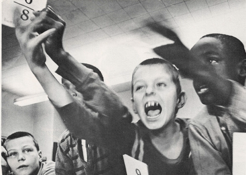 Black and white photo of young students yelling and reaching toward camera