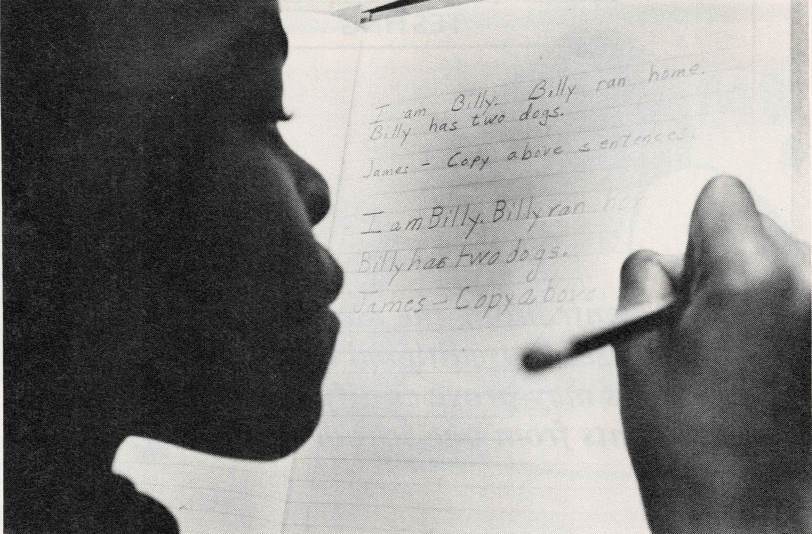 Black and white photo of young Black student writing on notebook paper