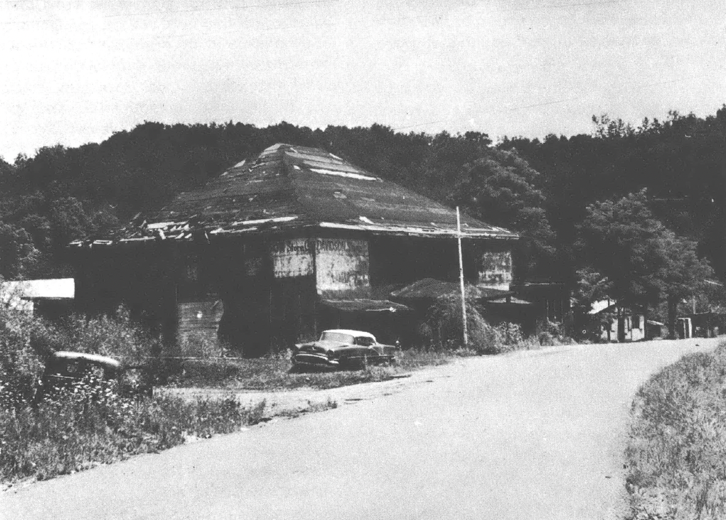 Black and white photo of building on side of the road with vehicle in front of it
