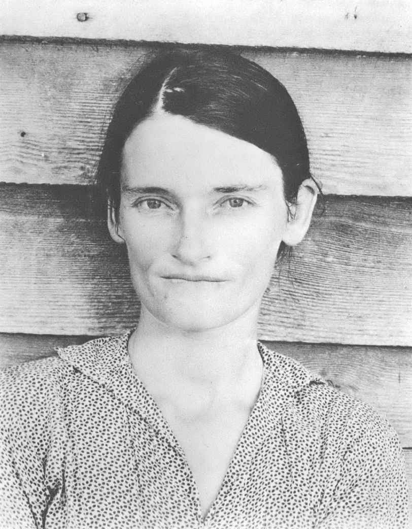 Black and white portrait of young white woman with hair pulled back standing against wood paneled building