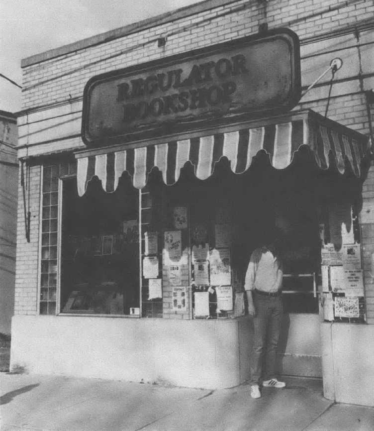 Black and white photo of front of Regulator Bookshop with awning and man standing in front of doorway