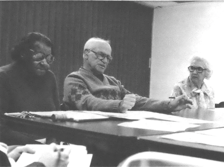 Photo of a Black man, a white man, and a white woman sitting in a meeting at a table