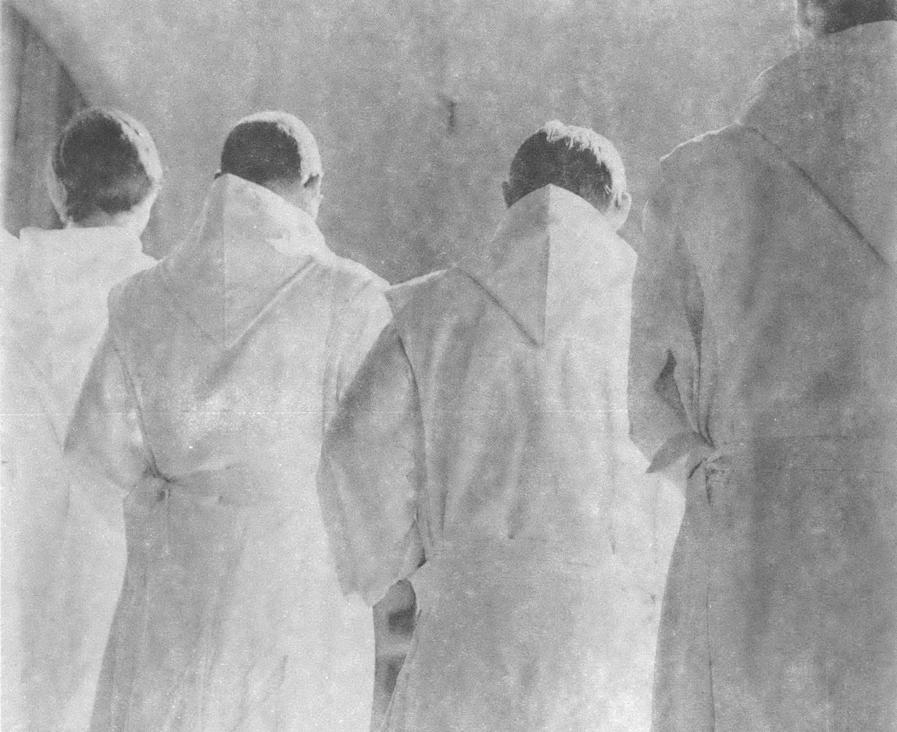 Black and white photo of three priests in white robes with back turned to camera