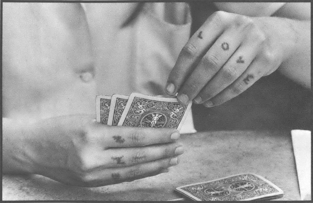 Black and white photo close-up of hands with tattooed knuckles holding a hand of cards