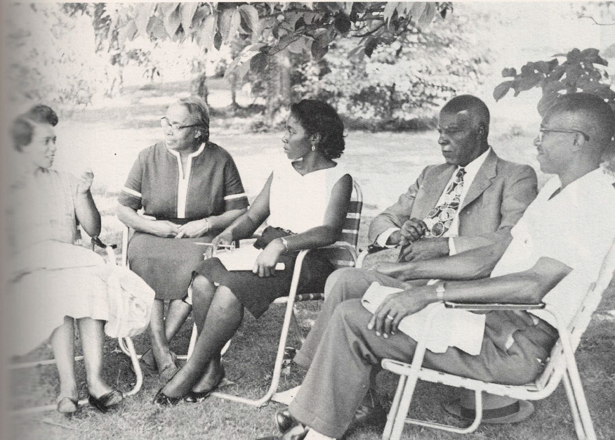 Black and white photo of group of people sitting in a circle outside