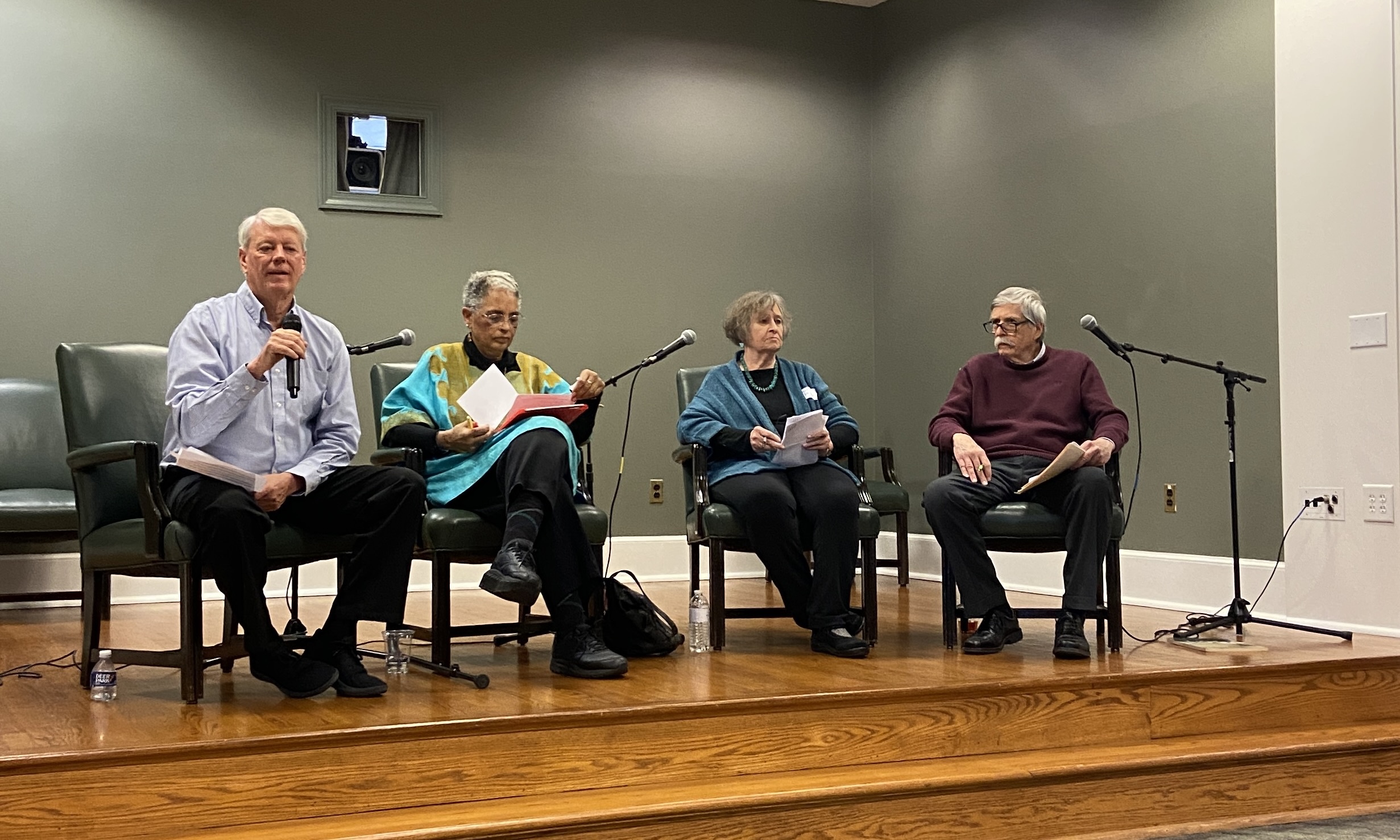 Four people sit on a stage in front of microphones