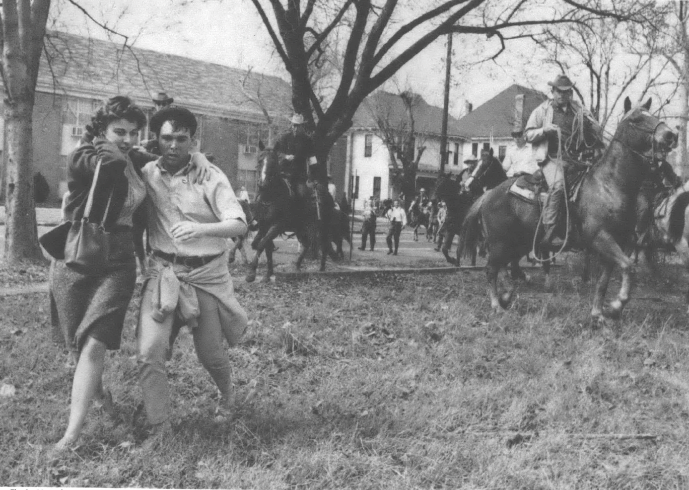 Black and white photo of people running from cops on horseback in a neighborhood