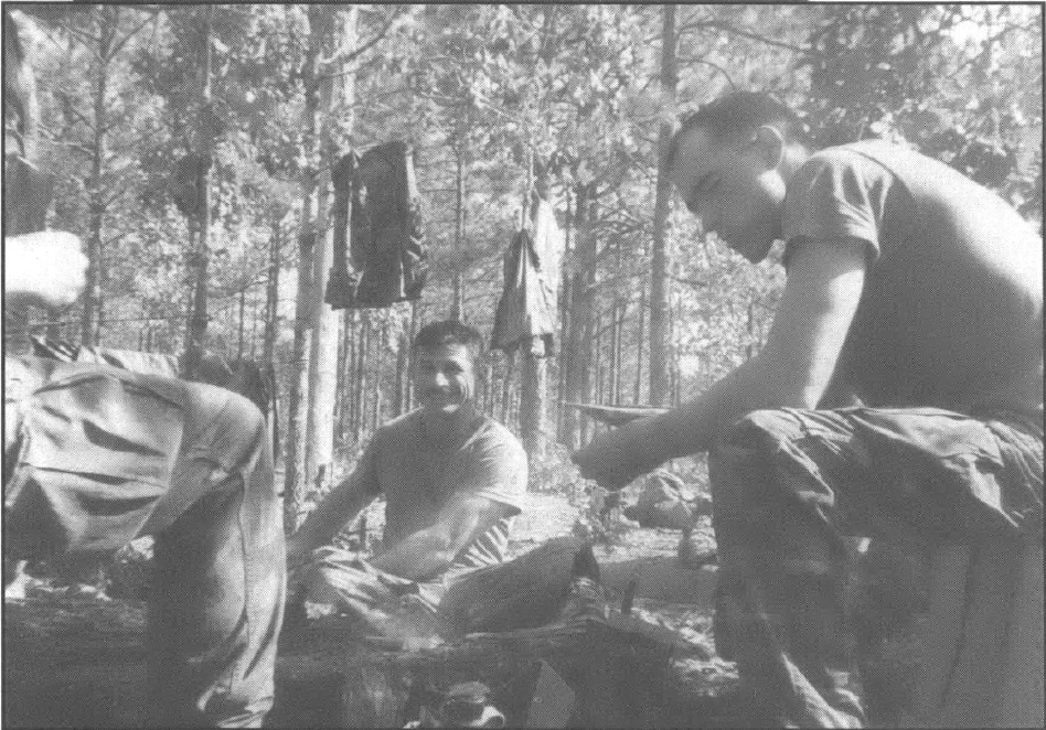 black and white photo of two white men in army wear in a forest next to a fire