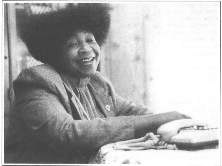 Photo of young Black woman seated at the table and laughing into the camera