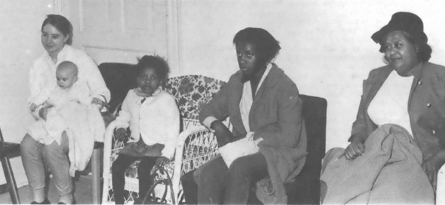Black and white photo of five people—a Black woman, two Black children, a baby, and a white woman—seated in a row.