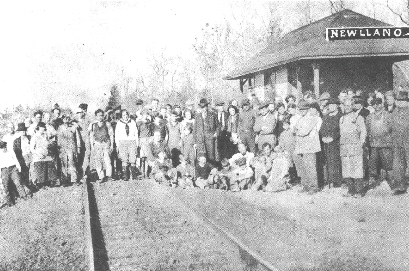 Black and white photo of crowd of people standing in front of railroad depot and across tracks