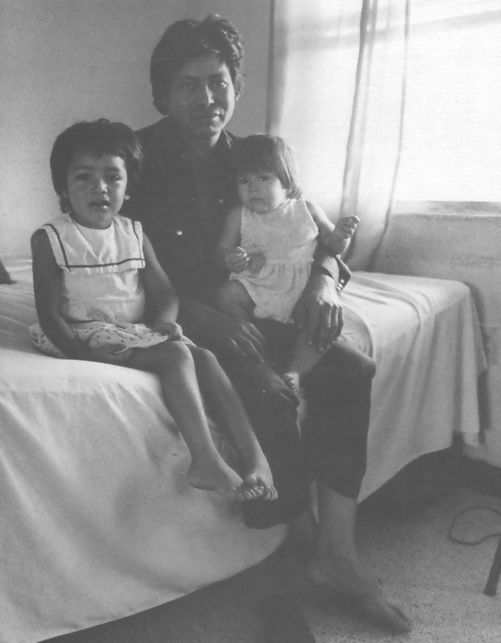 Black and white photo of man with two children sitting on bed