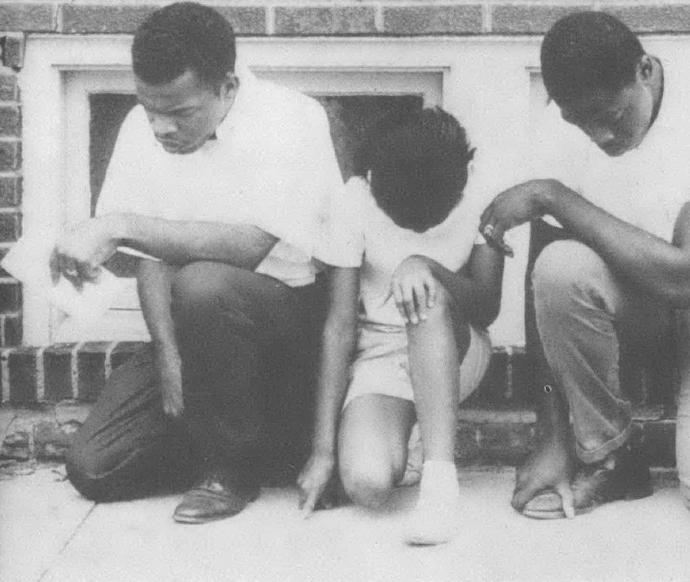 Black and white photo of a young John Lewis and two other people kneeling on sidewalk