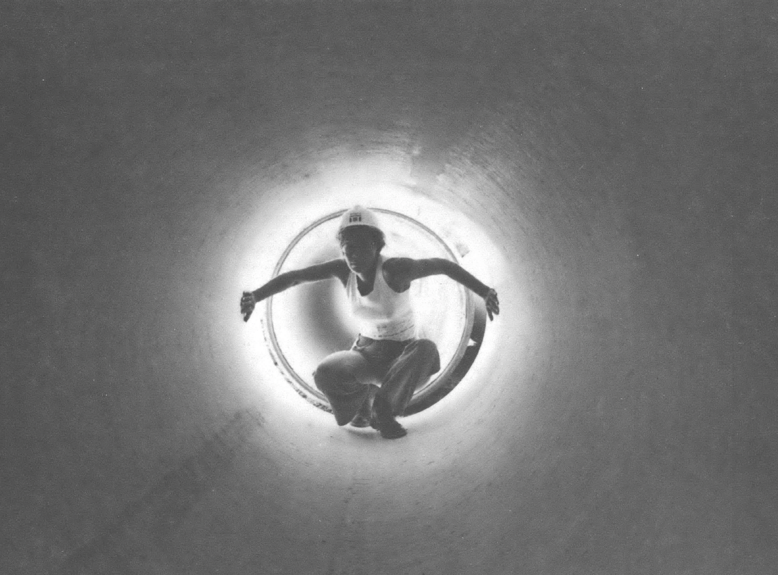 Black and white photo of woman in hard hat staring down pipe