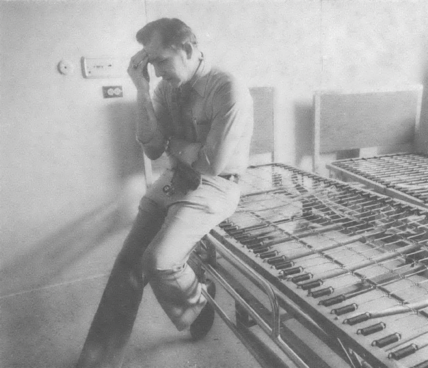 Black and white photo of man leaning against counter with hand on head