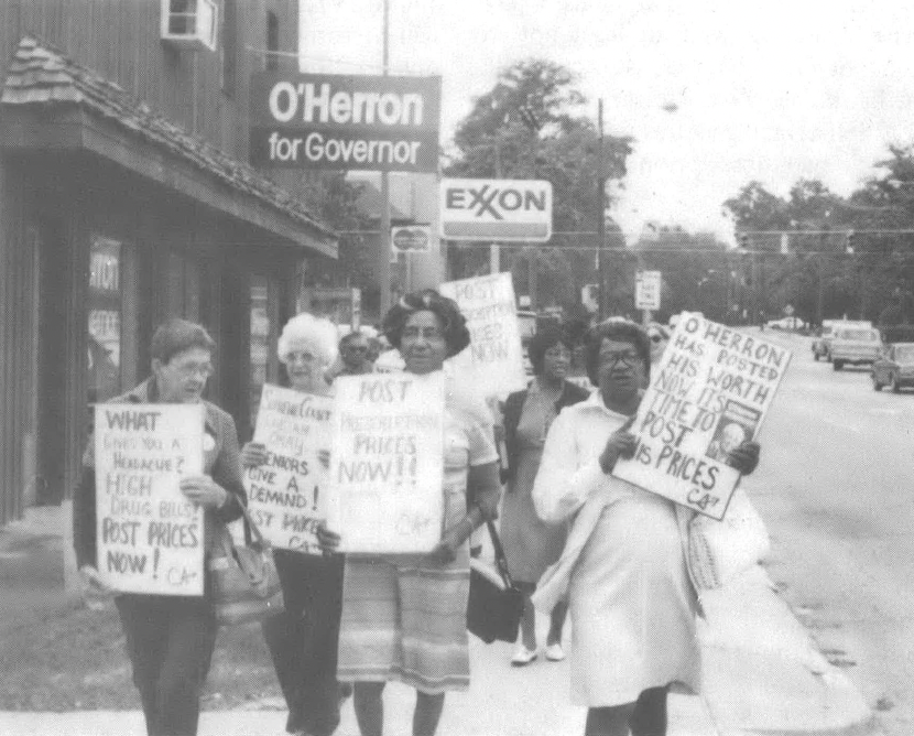 Black and white photo of people holding signs walking down a sidewalk