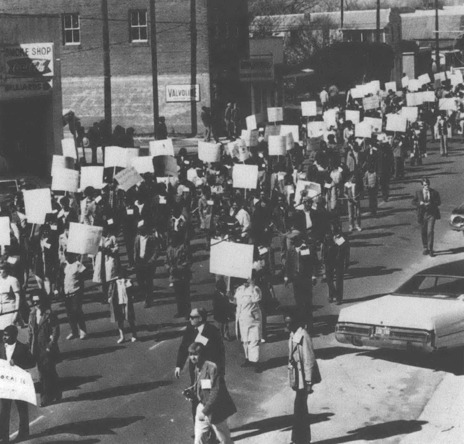 Black and white aerial view of protestors with signs marching down a street