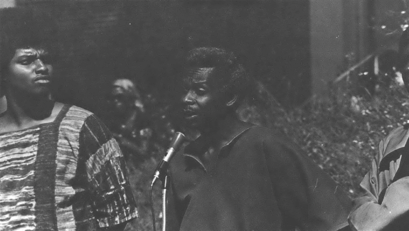 Black man speaks at a microphone as others look on