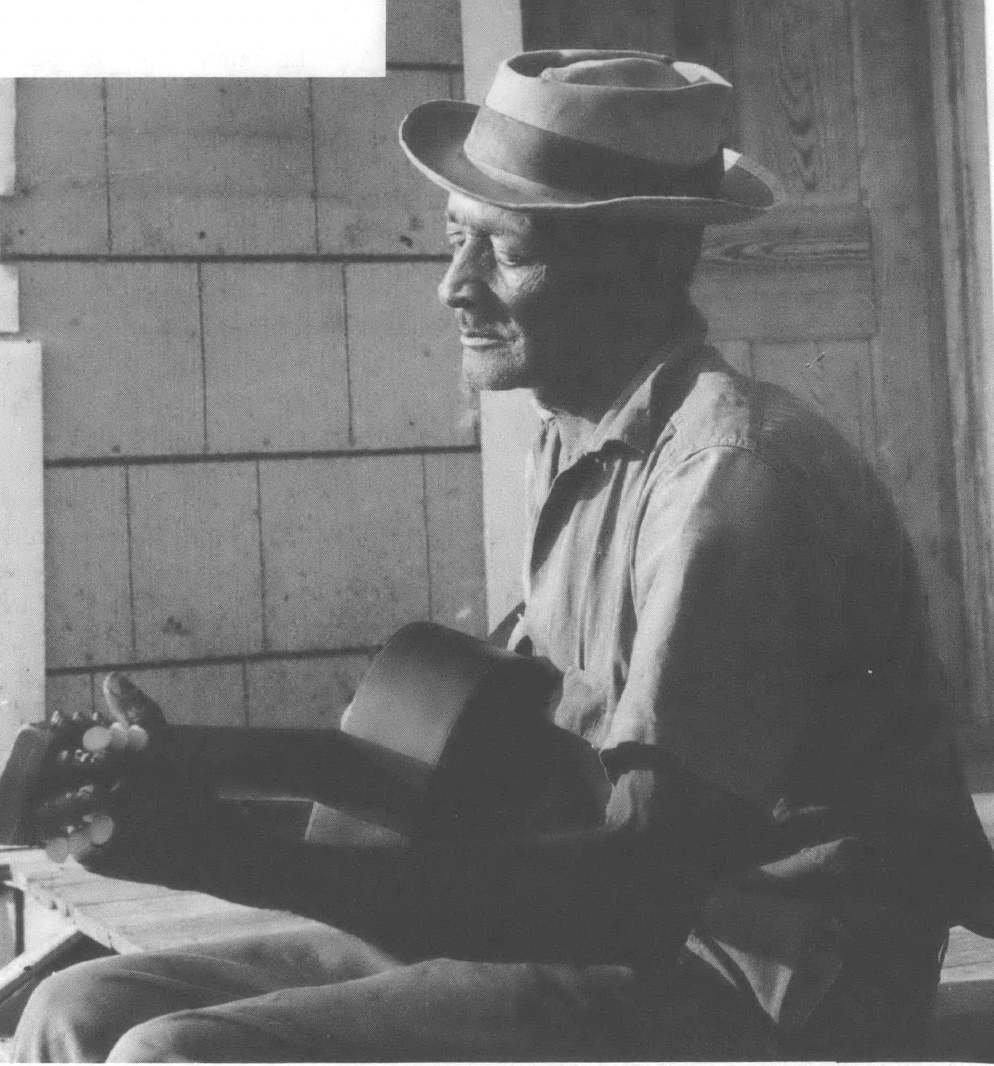 Black and white photo of Black man in hat playing guitar