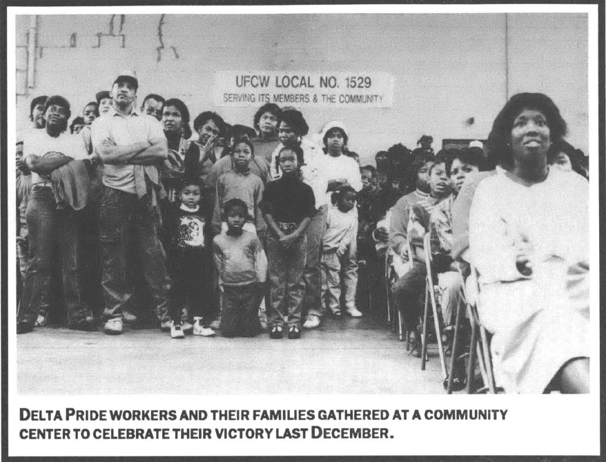 Delta Pride workers and their families at a community center sitting and standing in an auditorium a sign on the wall reads "UFCW Local No. 1529 Serving its Members & the Community"