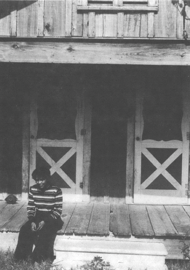Black and white photo of person sitting on steps of house