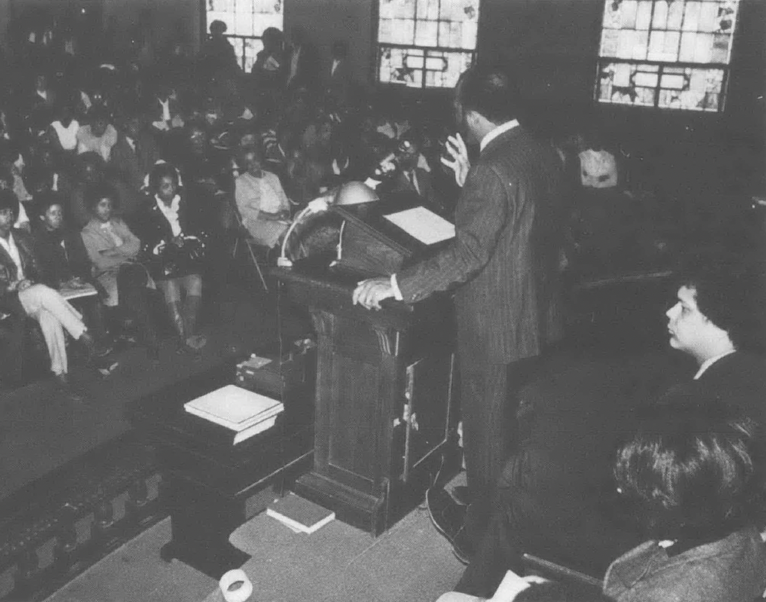 Black and white photo of John Lewis standing at podium speaking to a crowd of people in a church