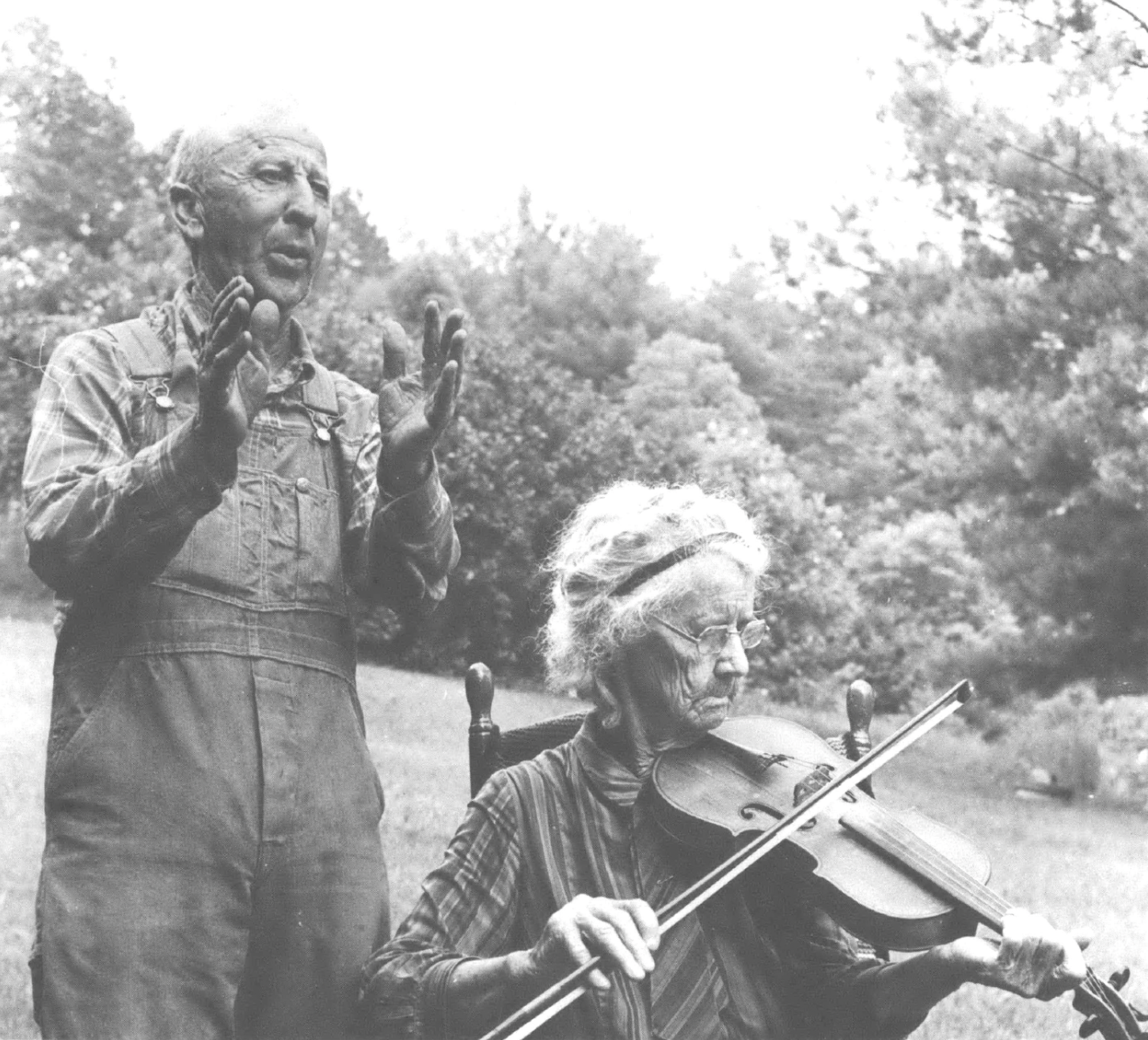 man clapping behind woman sitting and playing violin