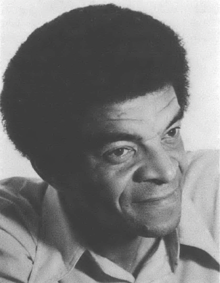 Black and white portrait of Black man smiling and looking at something outside the camera's lens