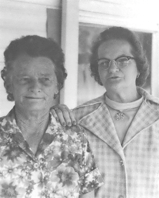 Black and white photo of two older white women, one shorter and one taller, in front of a house