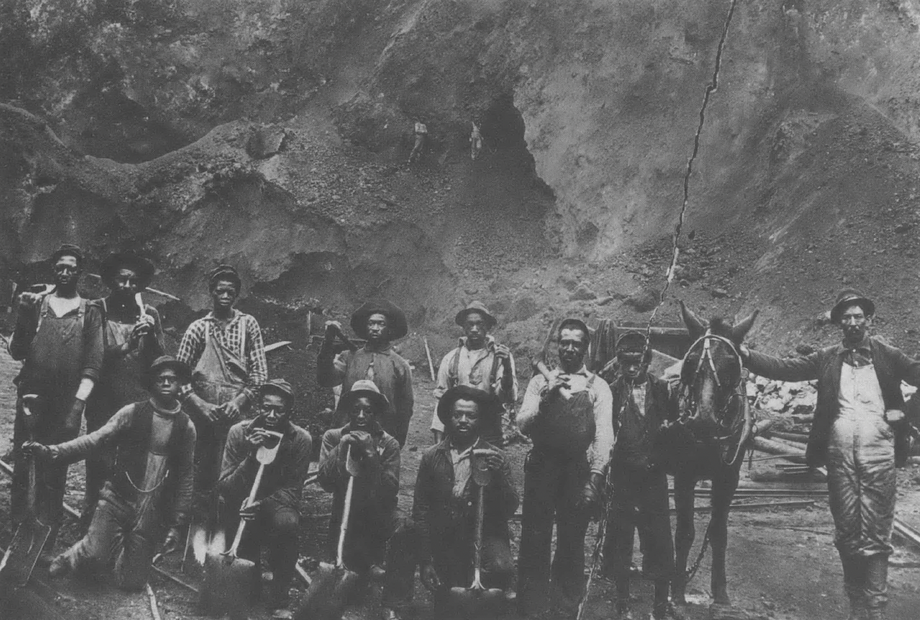 Black and white photo of about a dozen Black men in work clothes posing with tools