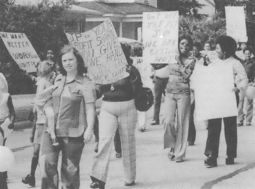 Black and white photo of several people marching down a street holding signs