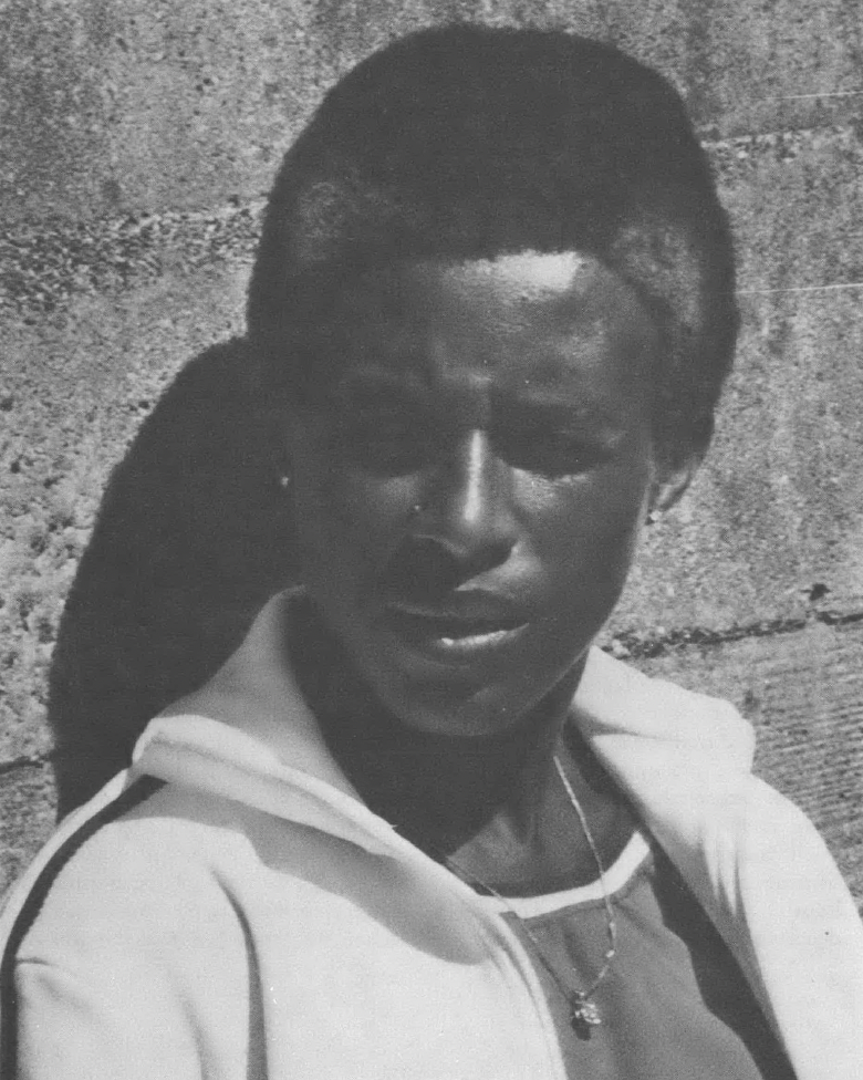 Black and white photo of Black woman with grey streaks in her hair leaning against a wall