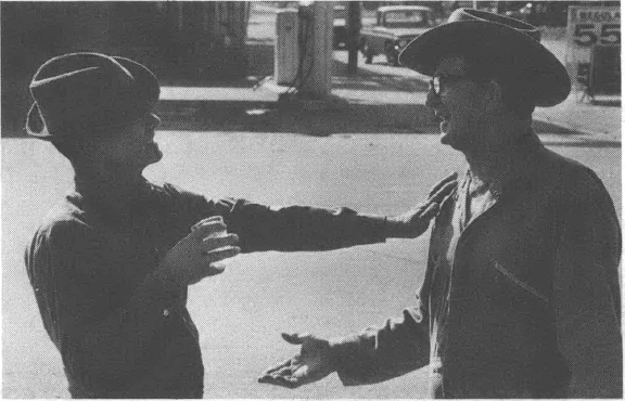 Black and white photo of two men in cowboy hats talking to each other on the street