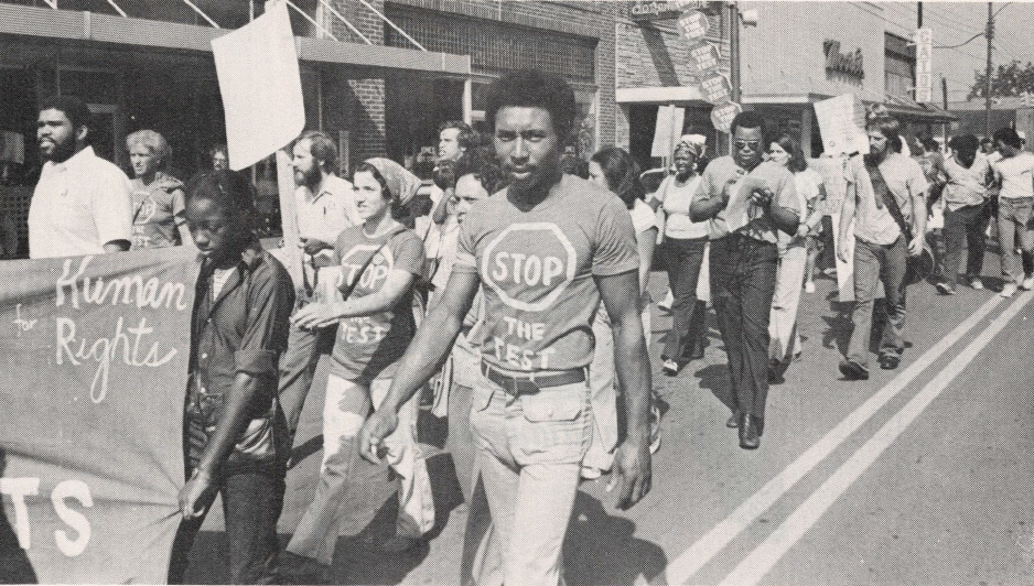 Black and white photo of people marching with banners and signs in the street