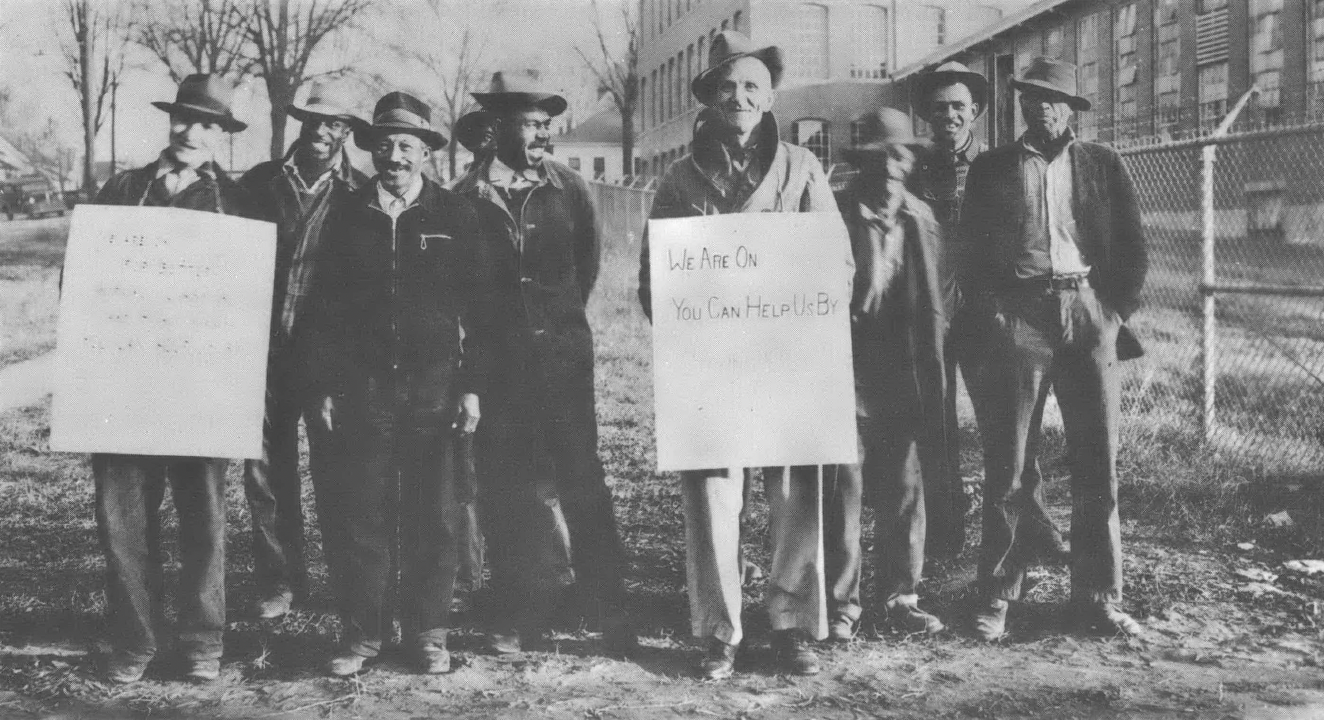 Black and white photo of group of men in bowler hats, some holding signs 