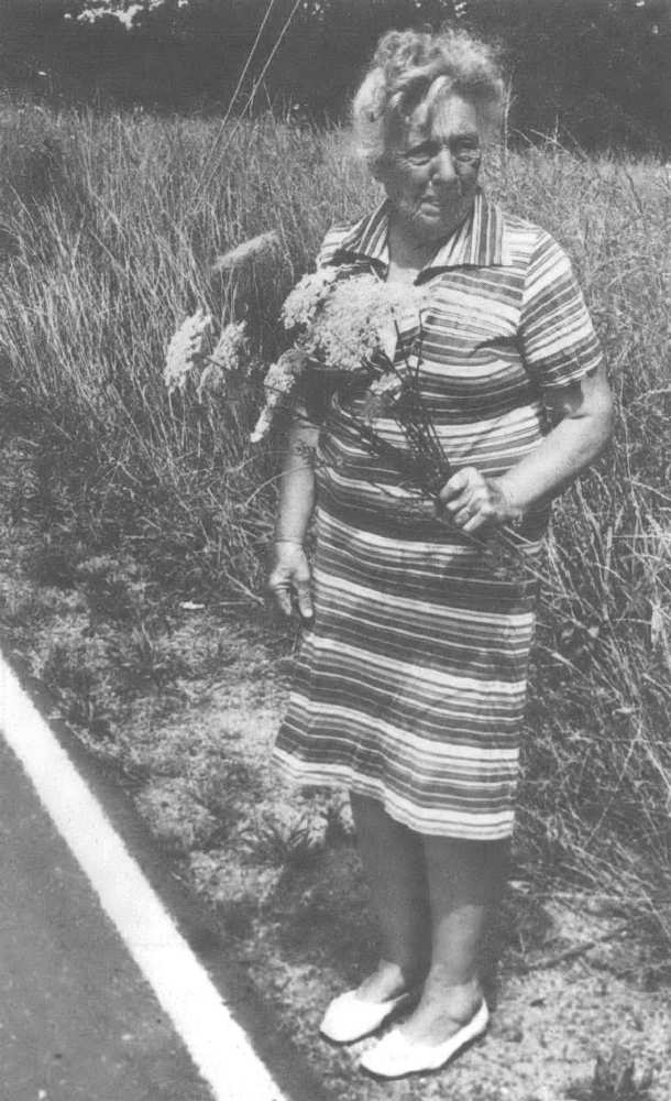 Black and white photo of woman in striped dress holding flowers and looking away from camera