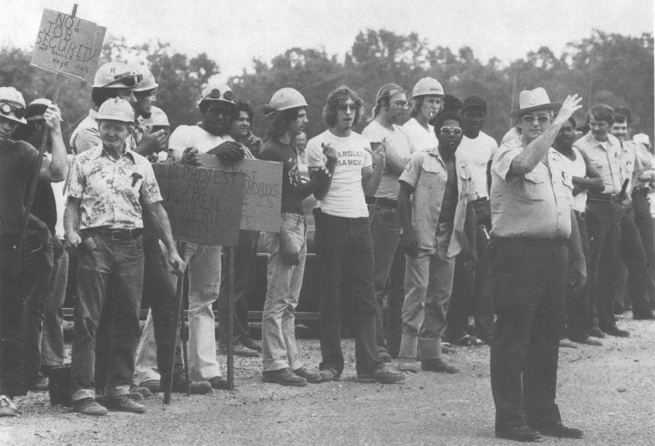 Black and white photo of group of picketers standing behind a uniformed man