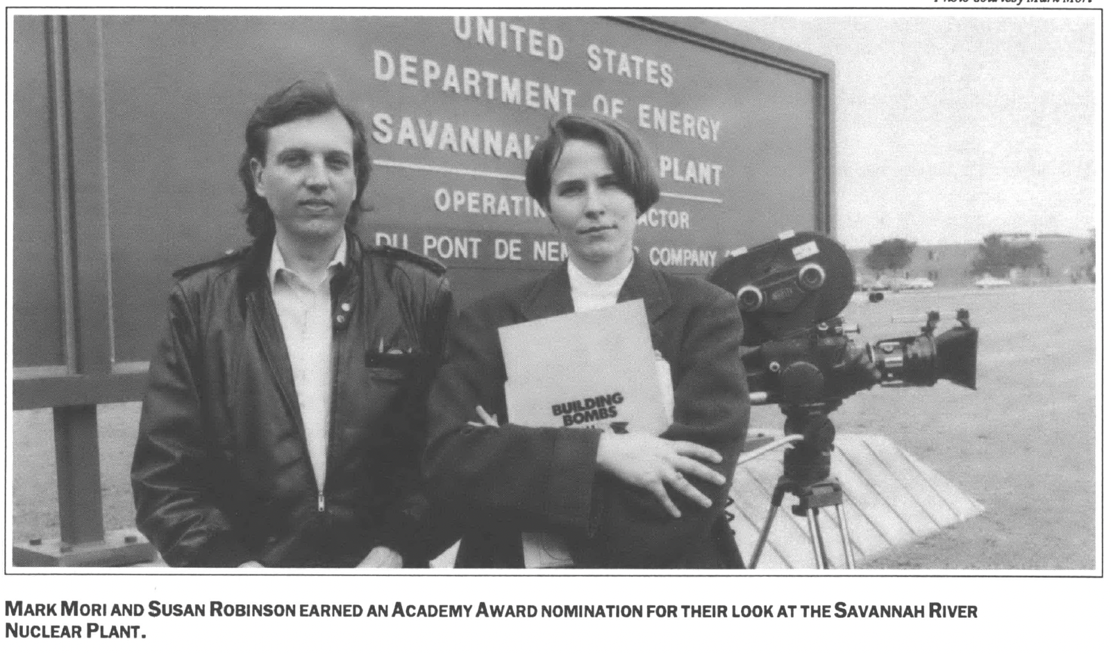 Two people and a camera in front of a US Department of Energy sign