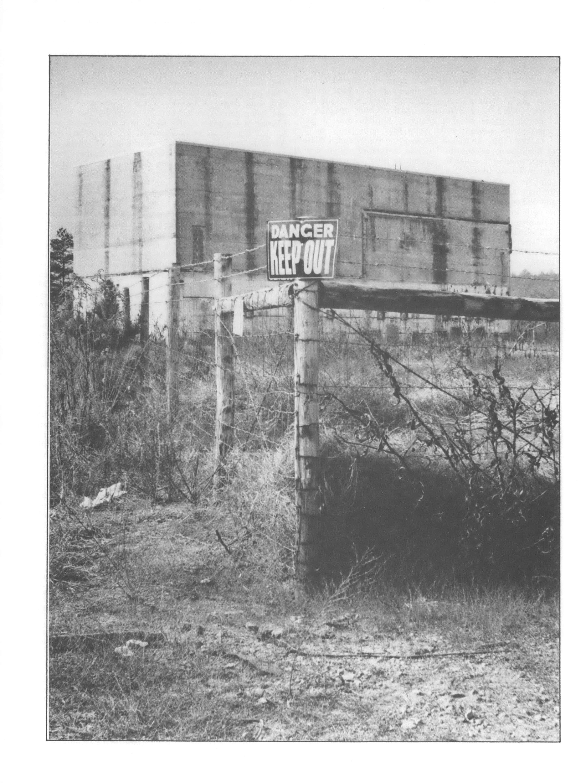 Black and white photo of fence with "keep out" sign