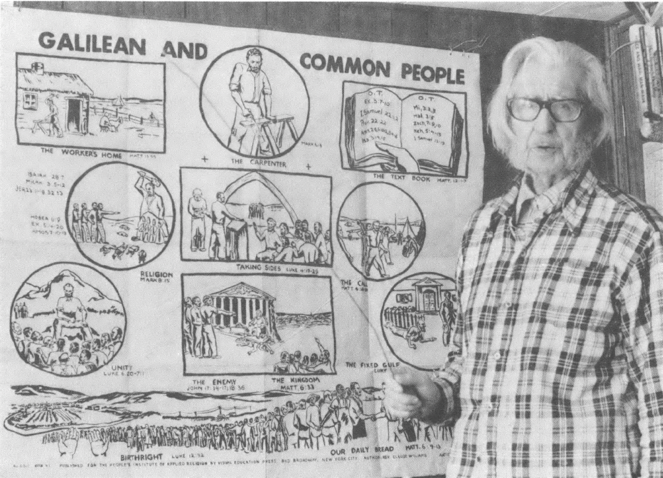 Black and white photo of older white man in glasses and plaid shirt standing in front of a large poster