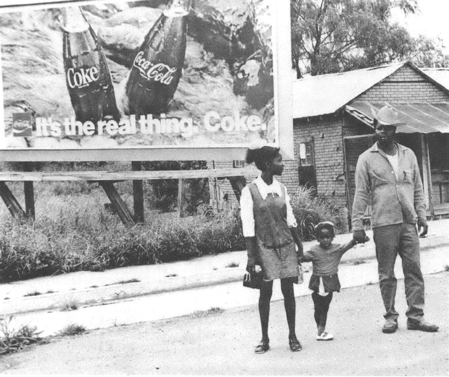 Black and white photo of Black family standing in front of Coke billboard
