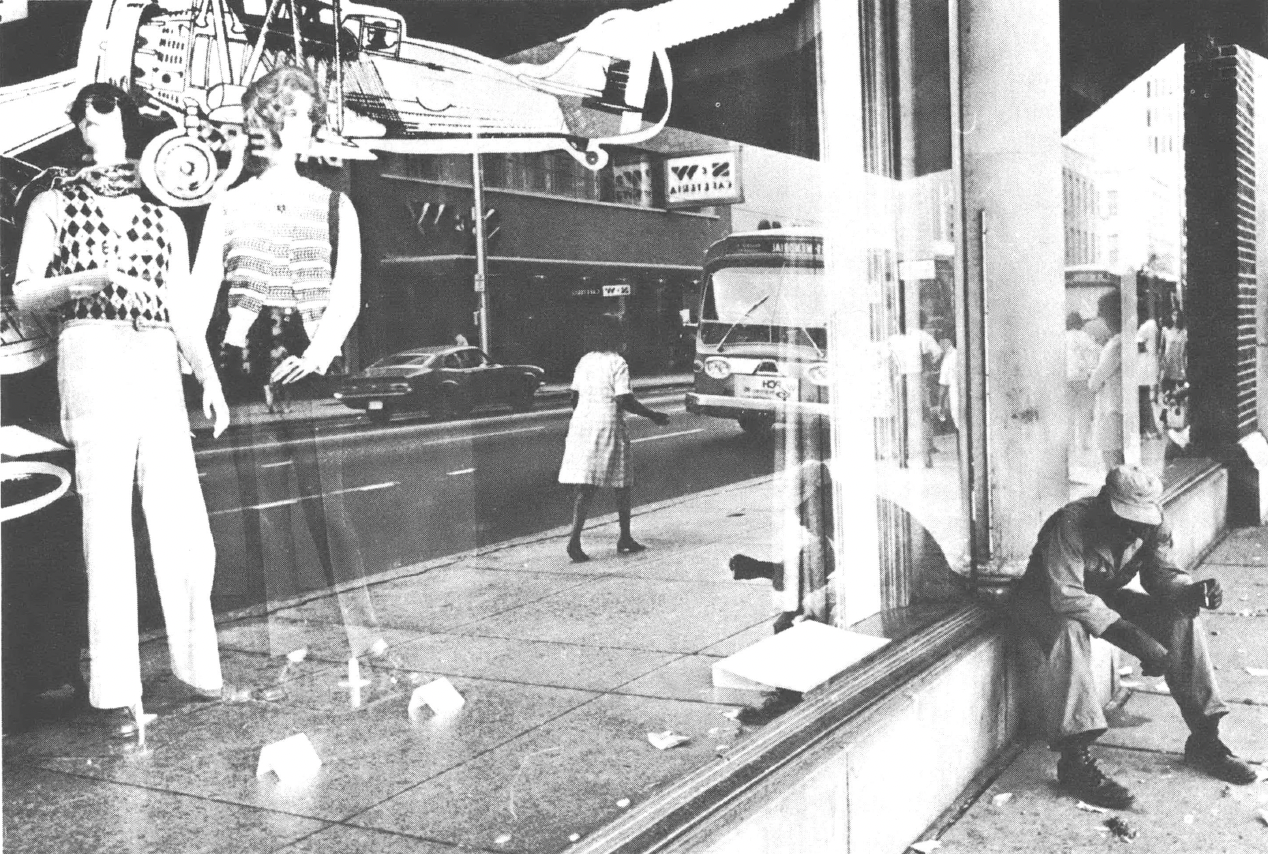 Streetscape with one person leaning in front of store window and one sitting by column