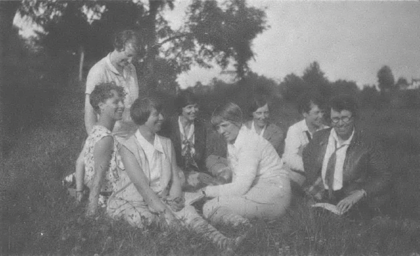 Black and white photo of group of women sitting in a circle outside