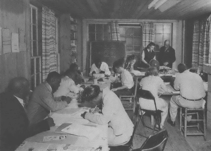 Black and white photo of people in a small schoolhouse room studying 