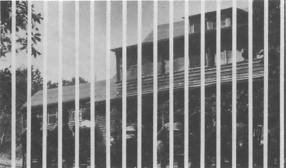 Black and white photo of rustic two-story wooden building behind graphic lines suggested prison bars
