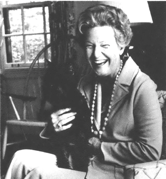 Mrs. Henry Cannon sitting in an armchair laughing and holding a small black dog