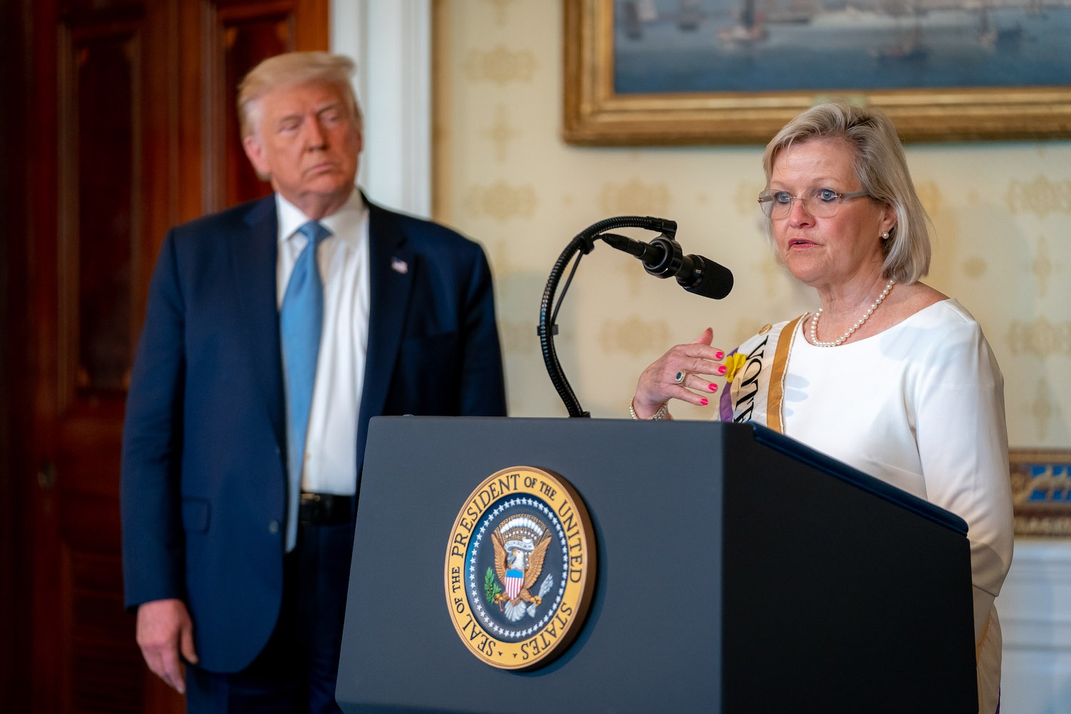 Cleta Mitchell talking at White House podium with President Trump standing behind her