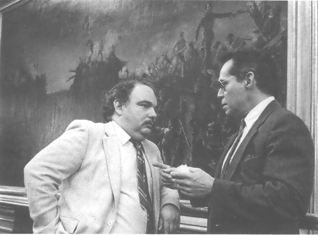Photograph of two men in suits talking to each other in front of large landscape painting