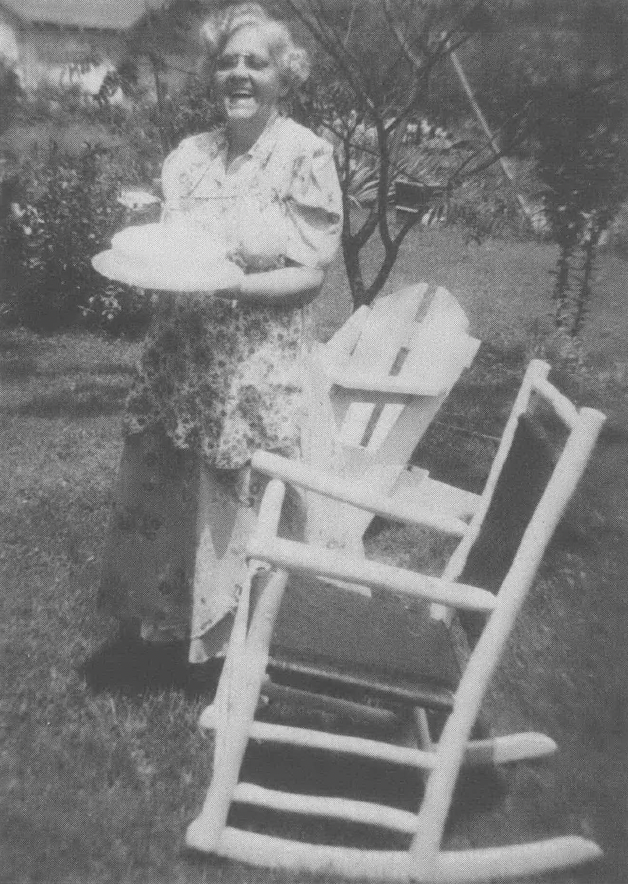 Black and white photo of elderly white woman standing outside next to rocking chairs
